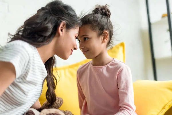 Amorosa madre e hija mirándose y tocándose la frente en casa - foto de stock