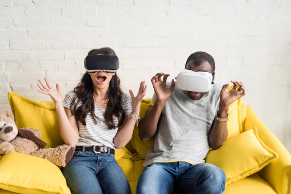 Scared african american couple in virtual reality headsets sitting on couch — Stock Photo