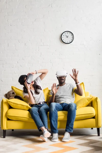 Expressive african american couple in virtual reality headsets sitting on couch — Stock Photo