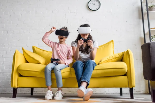 Mother and daughter in vr headsets playing video games at home on couch — Stock Photo