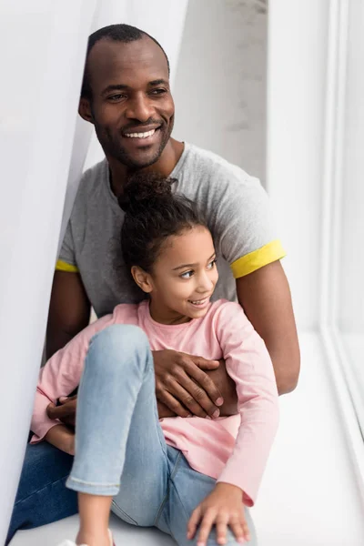 Sonriente afroamericano padre e hija sentado en alféizar de la ventana - foto de stock