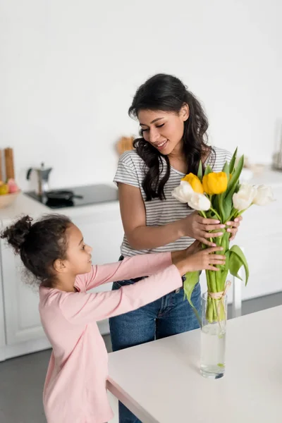 Young mother and beautiful daughter putting flowers into vase — Stock Photo
