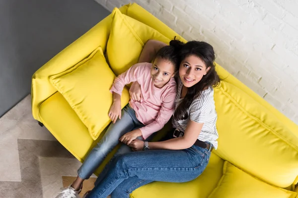 Вид сверху на мать и дочь, сидящие на диване вместе и смотрящие в камеру — стоковое фото