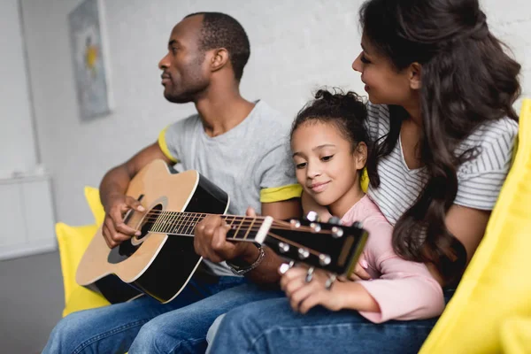 Мужчина играет на гитаре для жены и дочери дома — стоковое фото