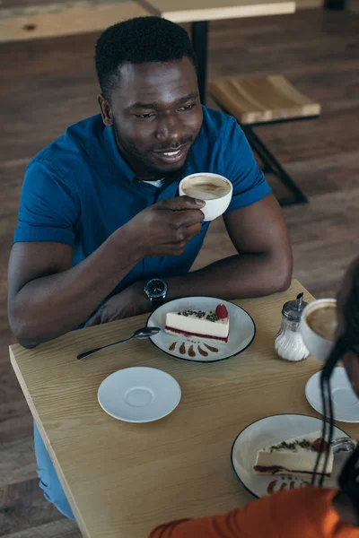 Vista de ángulo alto del hombre afroamericano sonriente con taza de café mirando a la novia en la cafetería - foto de stock