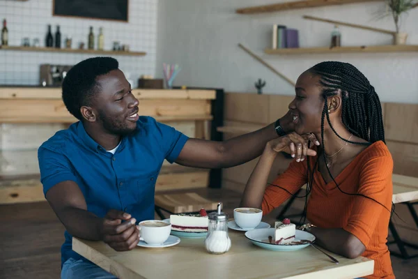 Heureux couple afro-américain assis à la table avec des tasses de café et desserts dans le café — Photo de stock