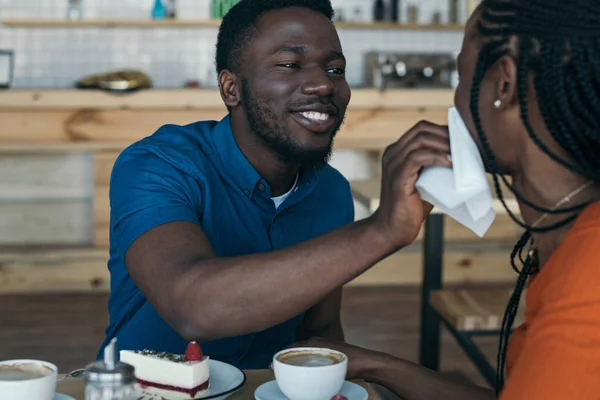 Careful african american man cleaning girlfriends face with napkin at table in cafe — Stock Photo