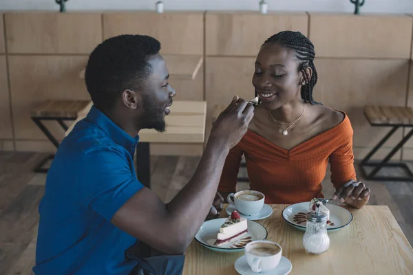 African american man feeding girlfriend with dessert on romantic date in cafe — Stock Photo