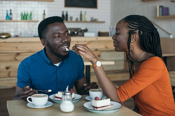 African american woman feeding boyfriend with dessert on romantic date in cafe — Stock Photo