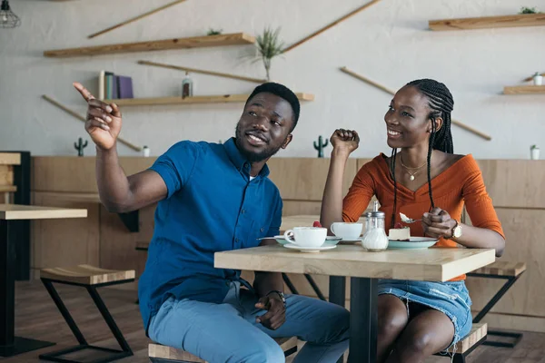 Африканская американская пара, сидящая за столом с чашками кофе и десертами в кафе — стоковое фото