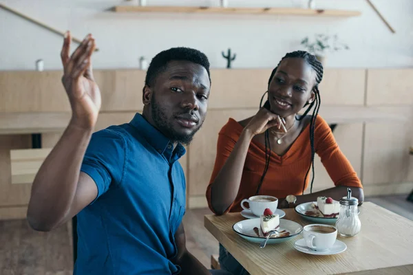 Африканская американская пара, сидящая за столом с чашками кофе и десертами в кафе — стоковое фото