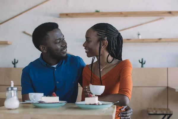 Ritratto di coppia afro-americana che si guarda mentre si siede a tavola con tazze di caffè e dessert nel caffè — Foto stock
