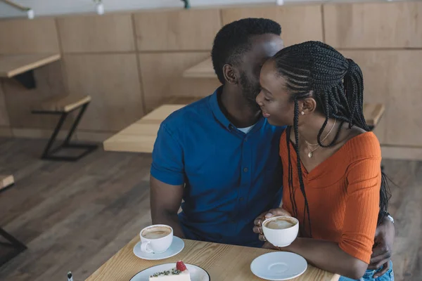 Tenera coppia afroamericana seduta a tavola con tazze di caffè e dessert nel caffè — Foto stock