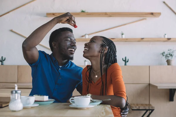 Afrikanisch-amerikanischer Mann füttert Freundin mit Erdbeere am Tisch im Café — Stockfoto