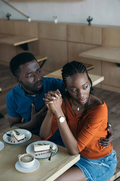 Vista de ángulo alto de la mujer afroamericana insultada con novio sentado en la mesa en la cafetería - foto de stock