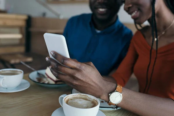 Recortado disparo de pareja afroamericana usando teléfono inteligente juntos en la cafetería - foto de stock