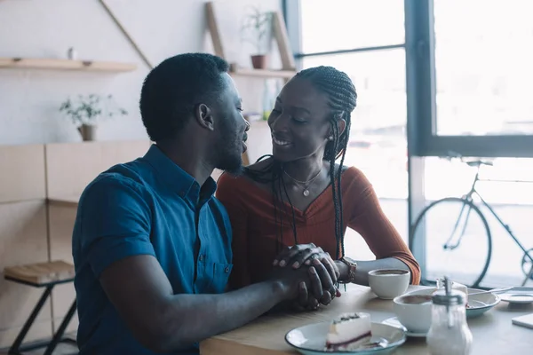 Sorridente coppia afro-americana che si tiene per mano e si guarda in appuntamento romantico in caffetteria — Foto stock