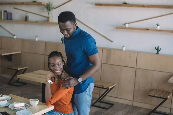 Sorridente africano americano uomo abbracciare fidanzata su appuntamento romantico in caffetteria — Foto stock