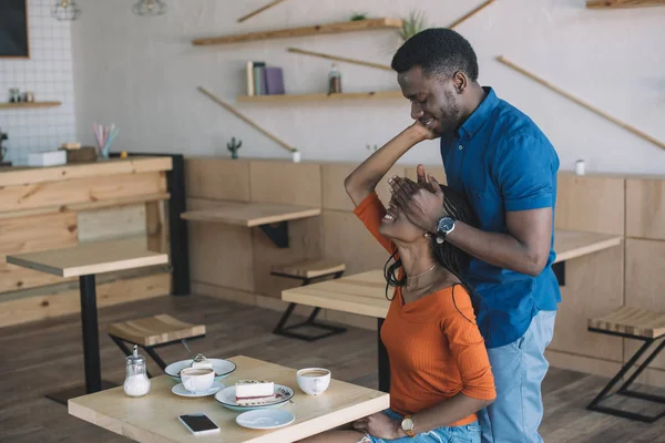 African american man covering girlfriends eyes to surprise her in coffee shop — Stock Photo