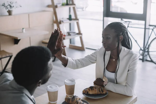 Afro-americanos amigos dando chocar los cinco unos a otros en la mesa en la cafetería - foto de stock