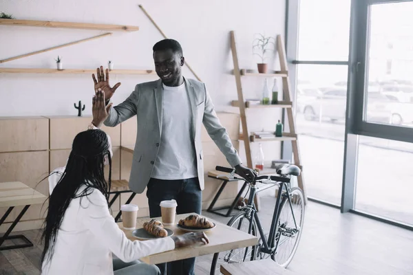 Amici afro-americani che si danno il cinque a vicenda a tavola in caffetteria — Foto stock