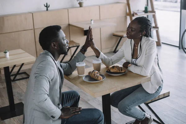 Afrikanisch-amerikanische Freunde geben einander am Tisch im Café High Five — Stockfoto