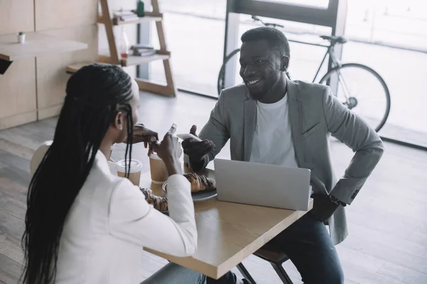 Vue partielle d'amis afro-américains assis à table avec ordinateur portable dans un café — Photo de stock