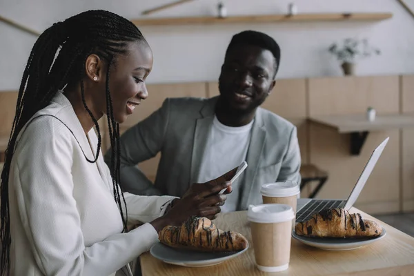 Amici afro-americani sorridenti seduti a tavola con laptop in caffetteria — Foto stock