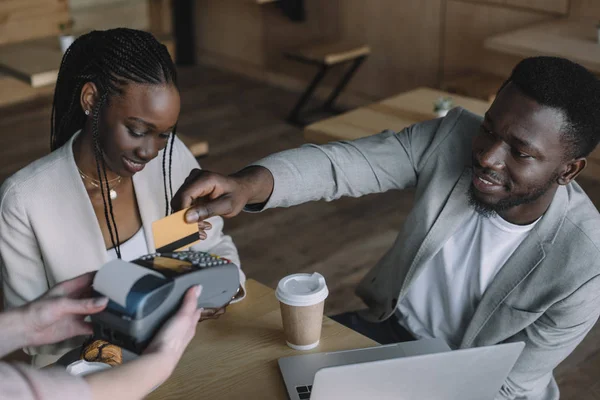 African american man paying for order with credit card while spending time with friend in cafe — Stock Photo