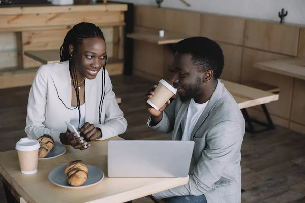 Африканские американские друзья сидят за столом с ноутбуком в кафе — стоковое фото