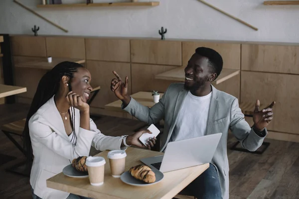 Amici afro-americani sorridenti a tavola con laptop in caffetteria — Foto stock