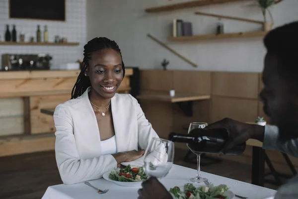 Vista parziale di afro americano versando vino nel bicchiere durante appuntamento romantico con la fidanzata nel ristorante — Foto stock