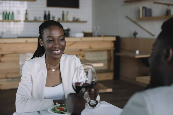 Vista parcial de pareja afroamericana tintineando copas de vino en restaurante - foto de stock