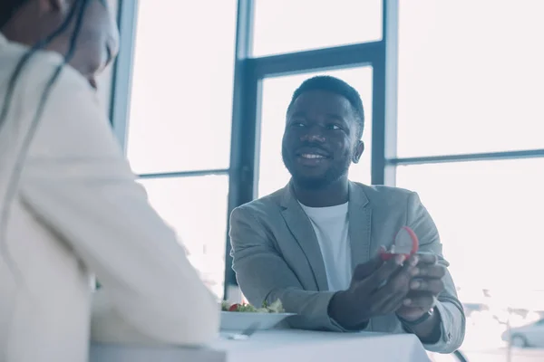 Vista parziale di un uomo afroamericano sorridente che si propone alla fidanzata durante un appuntamento romantico al ristorante — Foto stock