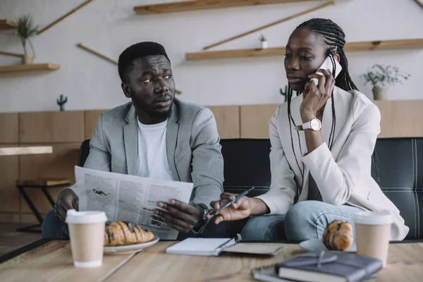 Африканская американская бизнесвумен разговаривает по смартфону во время деловой встречи с коллегой в кафе — стоковое фото