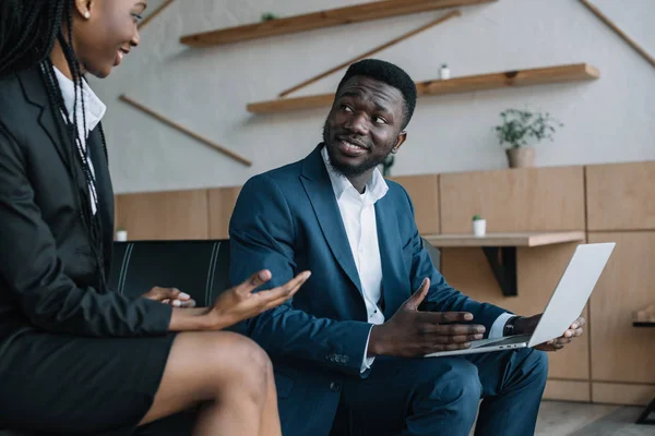 Uomo d'affari afroamericano sorridente con computer portatile e collega nelle vicinanze in caffè — Foto stock