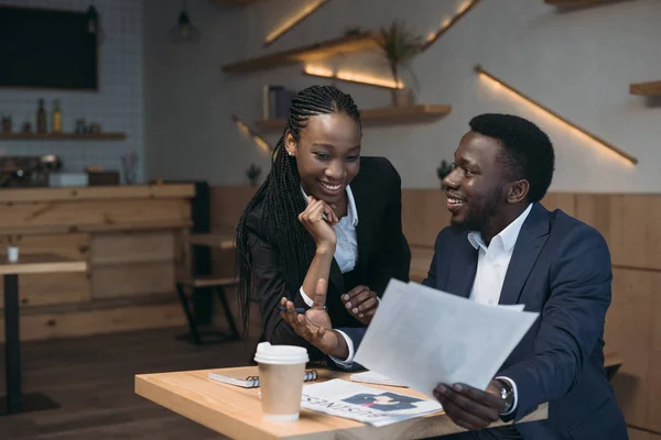 Sonrientes socios de negocios afroamericanos discutiendo proyecto sobre reunión en cafetería - foto de stock