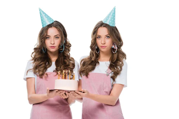 Atractivo jóvenes gemelos celebración de pastel de cumpleaños y mirando a la cámara aislada en blanco - foto de stock