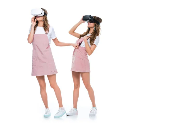 Gemelos sorprendidos viendo algo en auriculares de realidad virtual aislados en blanco - foto de stock