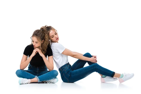 Привабливі молоді близнюки в джинсах і сорочках сидять на підлозі на білому — стокове фото