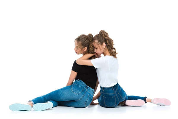 Вид сзади привлекательных маленьких близнецов, обнимающихся и сидящих на полу на белом — стоковое фото