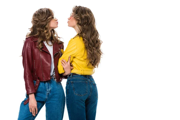 Вид сбоку привлекательных стильных близнецов в кожаных джинсах и солнцезащитных очках, собирающихся поцеловаться на белом фоне — стоковое фото