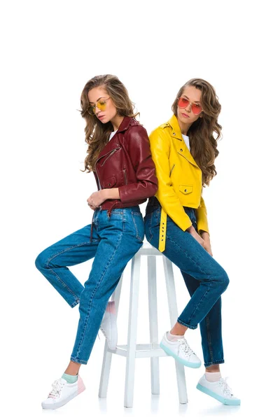 Attraenti gemelli eleganti in giacche di pelle e occhiali da sole seduti su una sedia di legno isolata su bianco — Foto stock