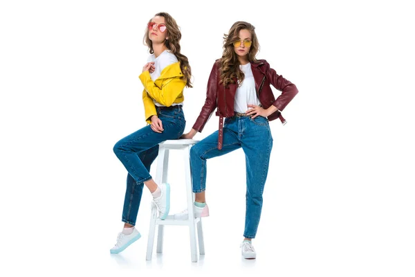 Attractive stylish twins in leather jackets and sunglasses with wooden chair isolated on white — Stock Photo