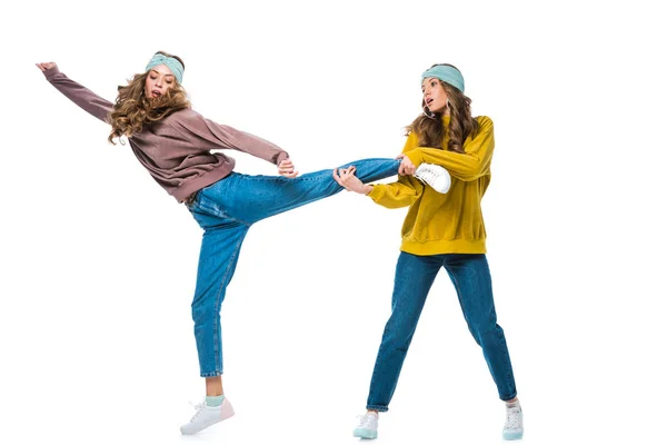 Atractivo joven gemelo celebración hermanas pierna aislado en blanco - foto de stock
