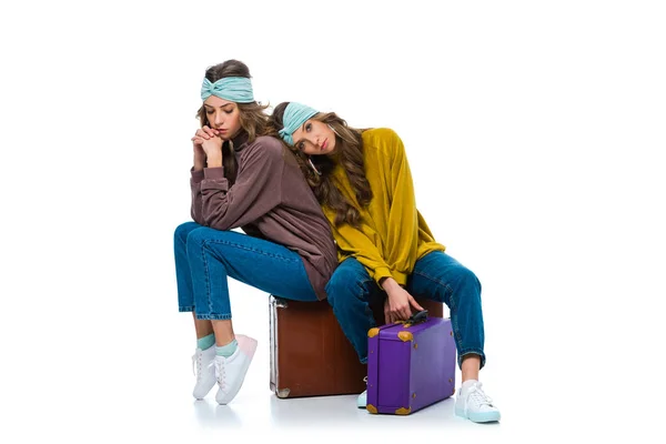 Attractive retro styled twins sitting on travel bags isolated on white — Stock Photo