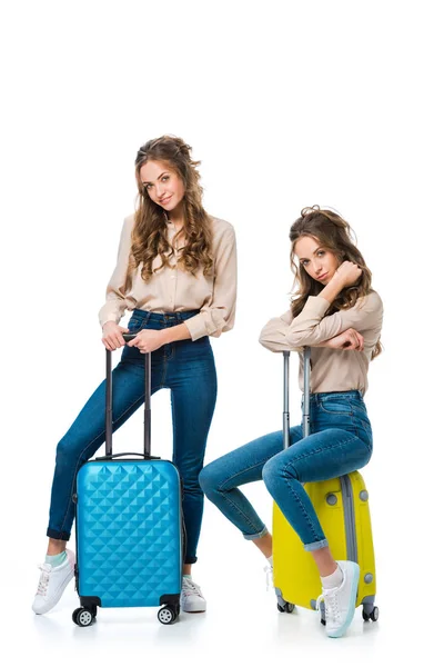 Attractive young twins with bags on wheels isolated on white, travel concept — Stock Photo