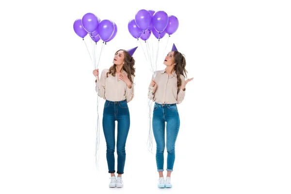 Surprised attractive young twins looking at violet balloons isolated on white — Stock Photo