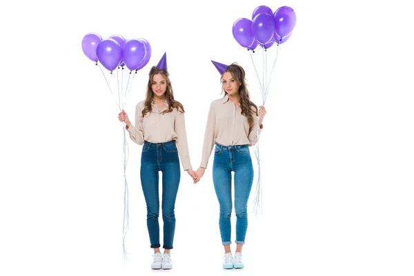 Attraktive junge Zwillinge mit violetten Luftballons, die die Hände isoliert auf weiß halten — Stockfoto