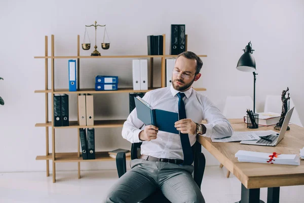 Porträt eines Rechtsanwalts mit Brille beim Lesen eines Buches am Arbeitsplatz im Büro — Stockfoto